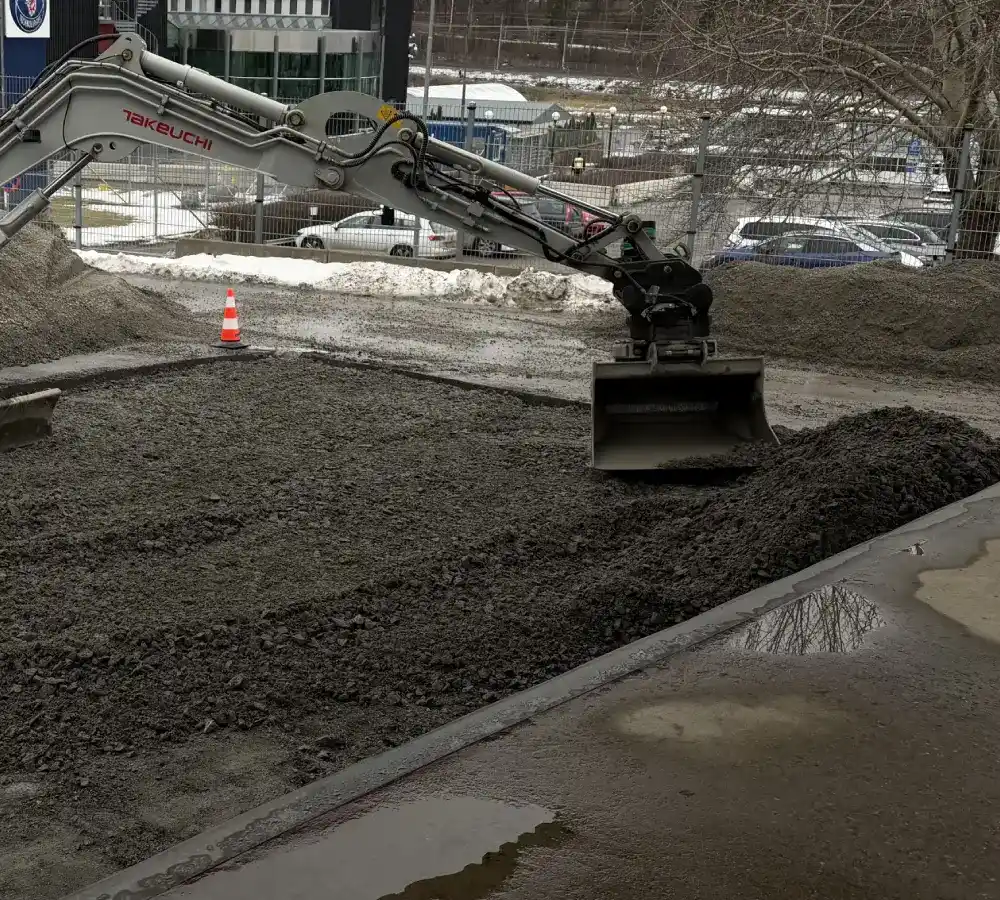 Grävmaskin jämnar ut bärlager av makadam inför grundläggning