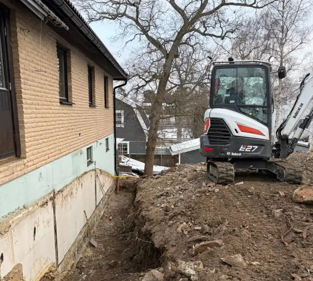 Minigrävare schaktar runt husgrund vid villa inför dränering