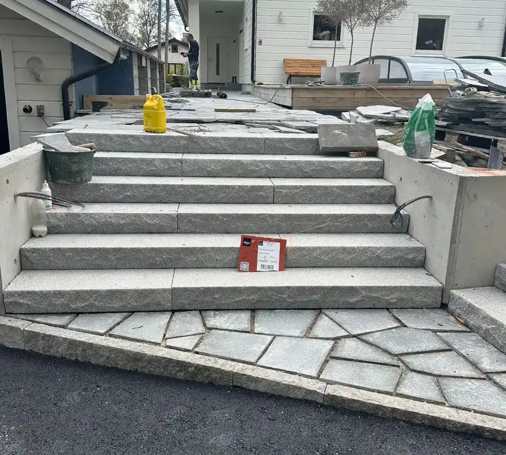 Stenläggning av natursten vid entré och trappa till villa under pågående arbete